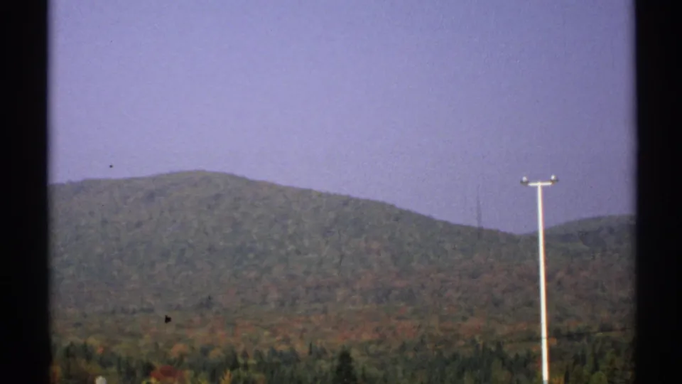 1971 New York 8mm view of wooded hills and fall foliage, partly obscured by dark frame edges and a utility pole.