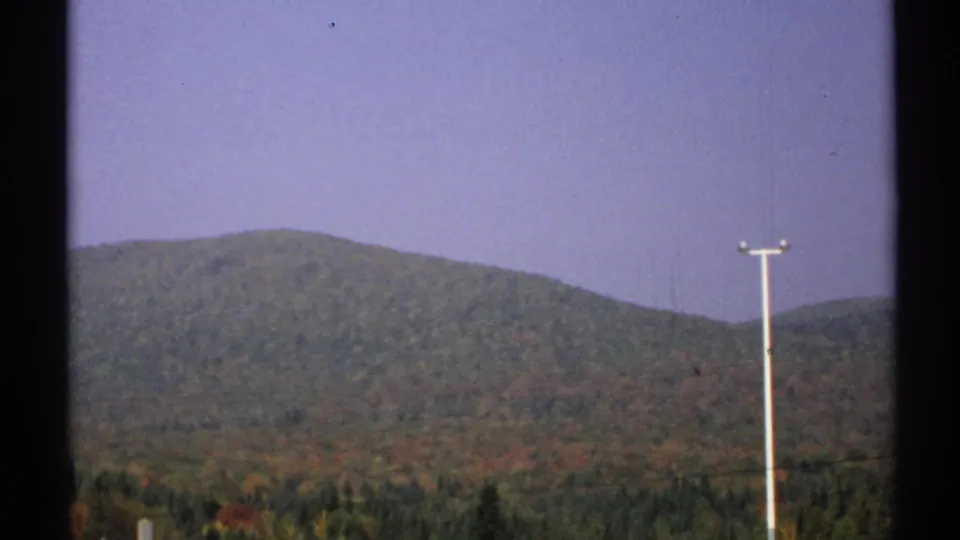 1971 New York 8mm frame showing wooded autumn hills, pale sky, a right-side utility pole, and dark framing edges.