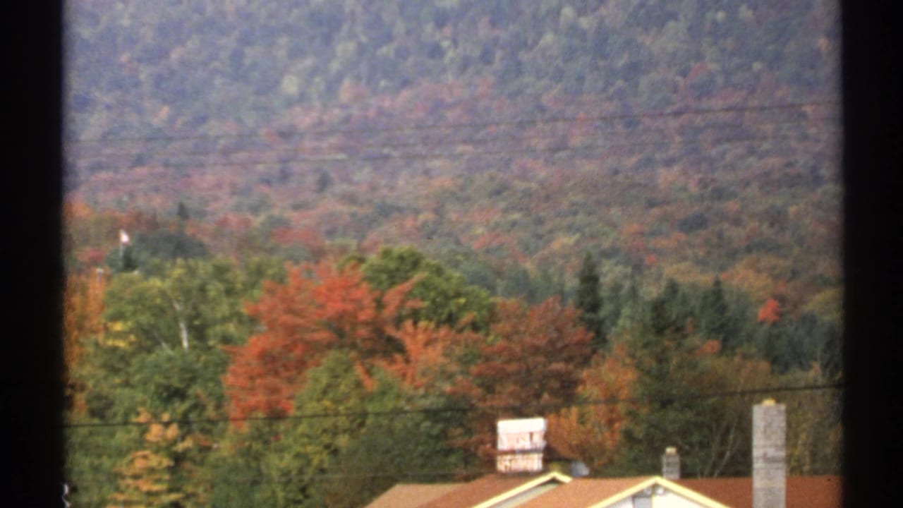 1971 New York 8mm view of fall foliage, overhead power lines, rooftops, and chimneys beneath wooded hills.