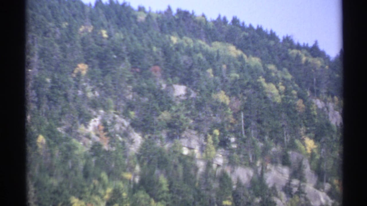 Soft 8mm frame of a New York mountainside, showing forest cover, exposed rock, and autumn-tinted trees.