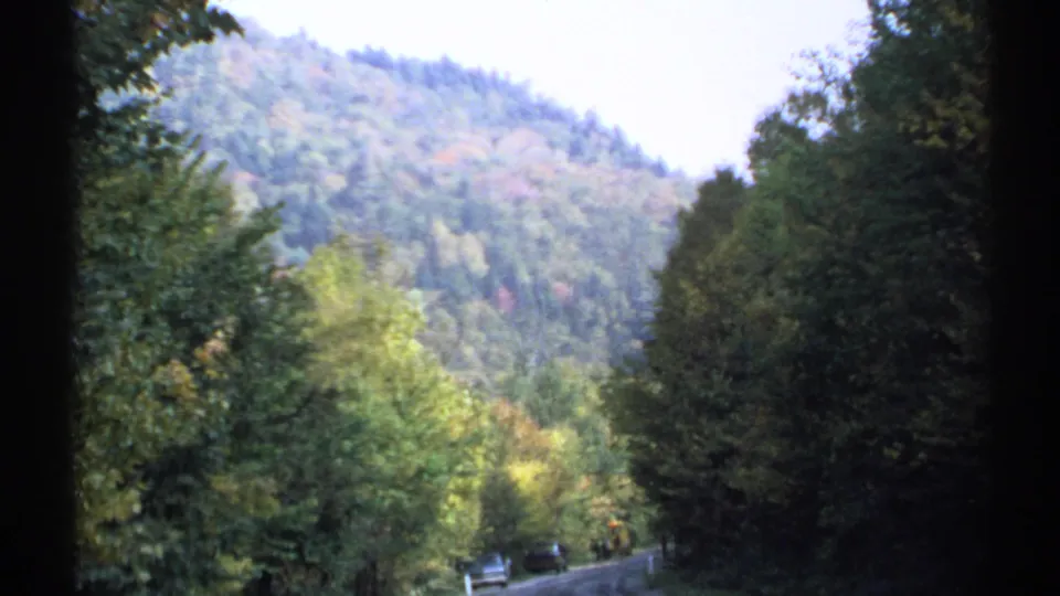 A 1971 New York 8mm frame shows autumn trees and a winding road with small cars below a wooded mountain.