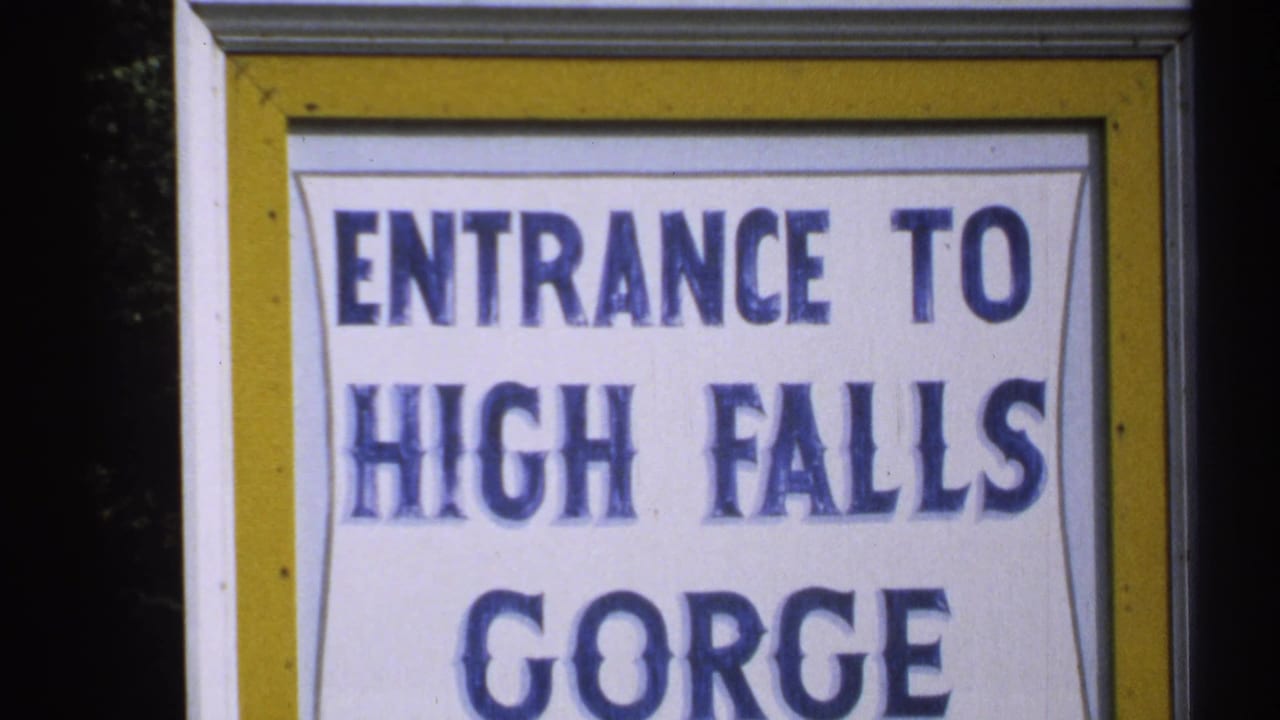 Close-up of a sign reading Entrance to High Falls Gorge with blue lettering and yellow border.