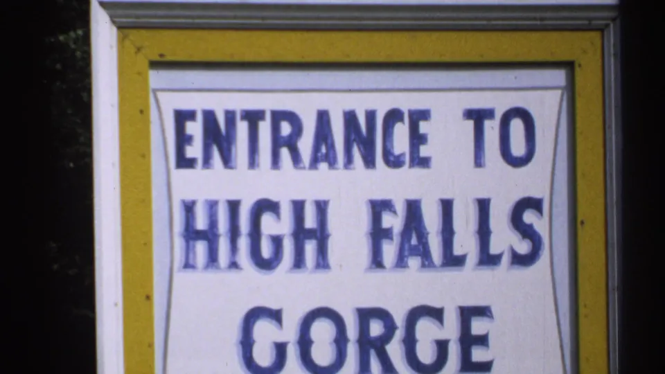 1971 New York 8mm frame showing a close-up of the Entrance to High Falls Gorge sign in blue letters on white.
