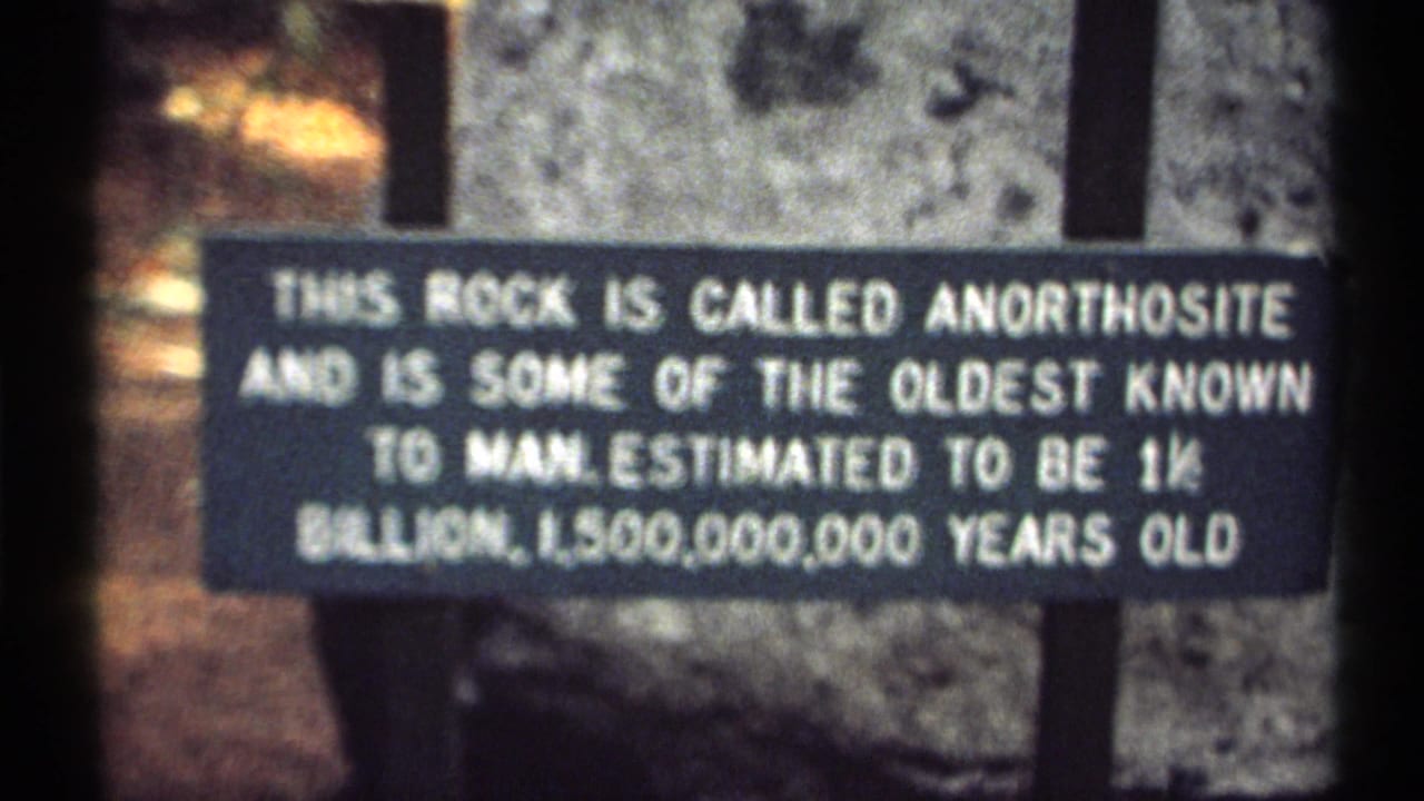 1971 New York 8mm frame showing a close view of an anorthosite rock sign against gray stone and dark supports.