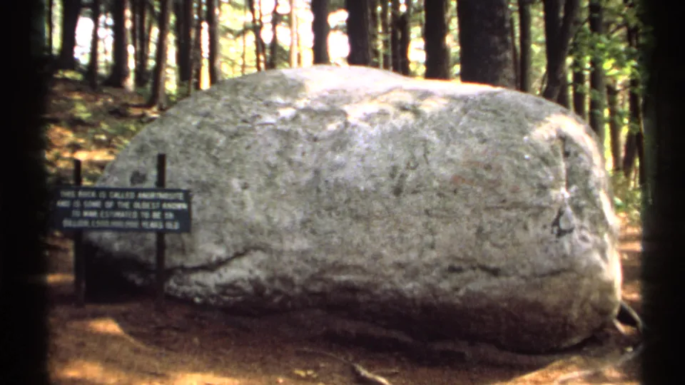Large anorthosite boulder and nearby sign appear in a wooded New York setting on 1971 home-movie film.