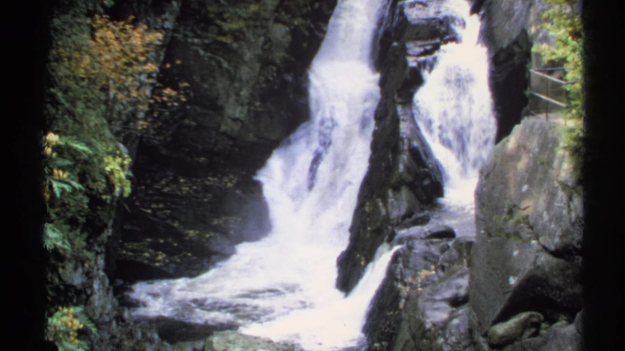 Waterfall and rocky gorge with a metal railing visible at the right edge.