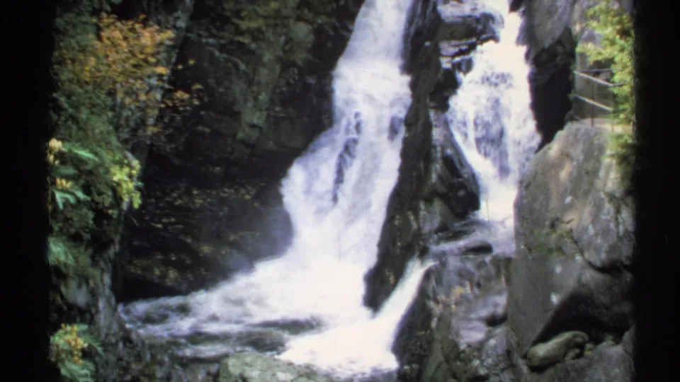 1971 New York 8mm frame with the waterfall filling more of the view as water rushes over dark stone ledges.