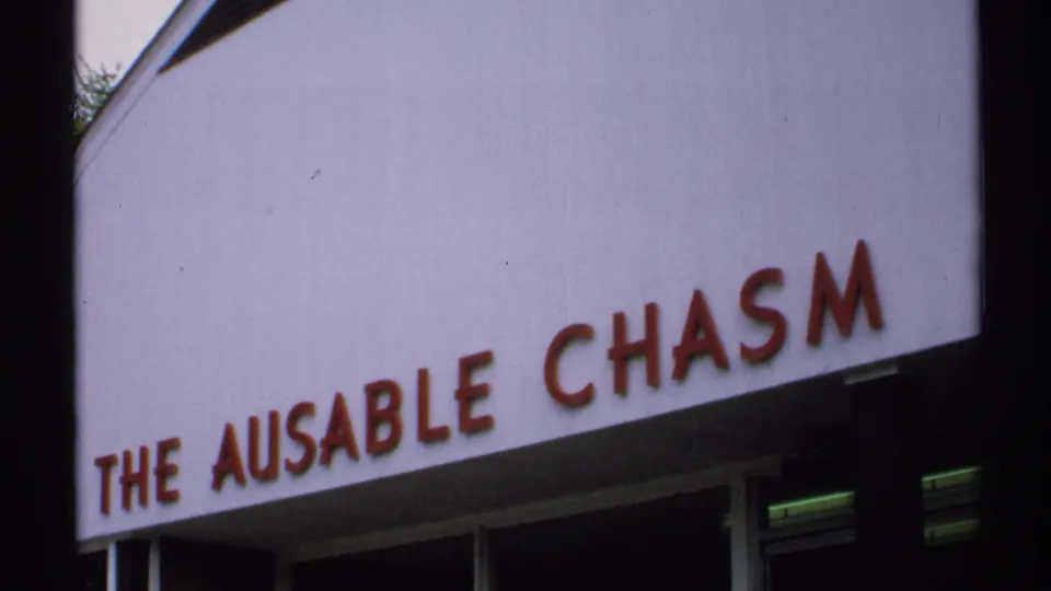 Vintage 8mm frame from New York, 1971, with the pale THE AUSABLE CHASM sign angled above dark window openings.