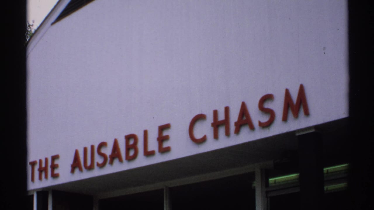 White sign reading THE AUSABLE CHASM with red letters and dark building edge.