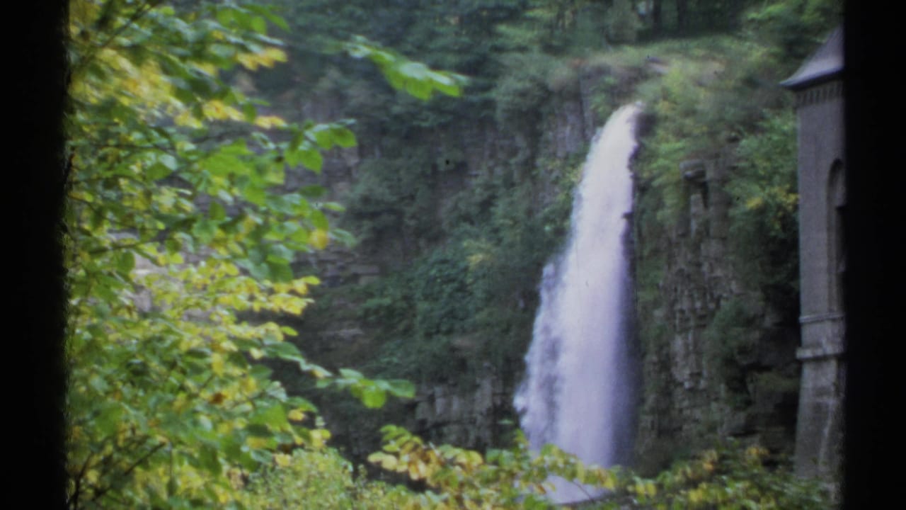 Waterfall dropping down a rocky cliff, framed by green leaves and dark film borders.