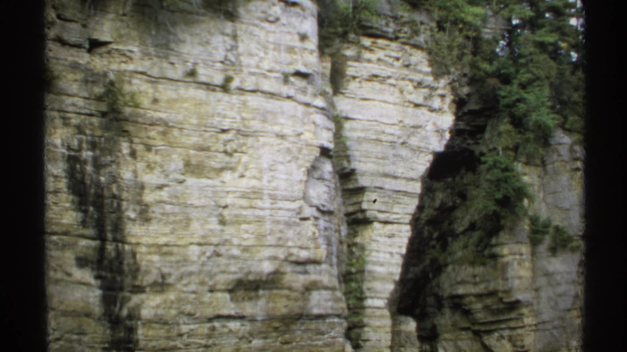 1971 New York 8mm frame showing a tall layered rock cliff, sparse greenery, and dark contact-sheet borders.