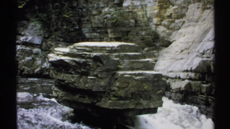1971 New York 8mm frame with a flat-topped rock shelf over whitewater, framed by gorge walls and vegetation.