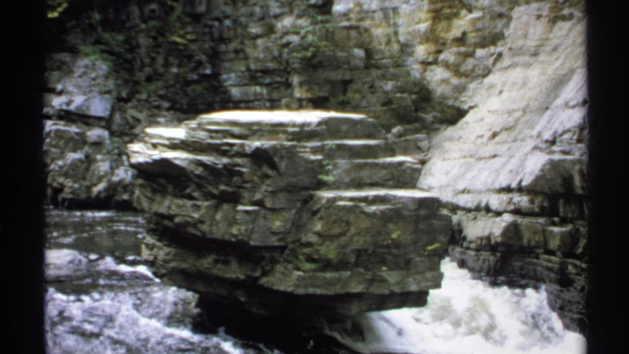 1971 New York 8mm frame showing white water cascading beside a broad layered boulder in a rocky gorge.