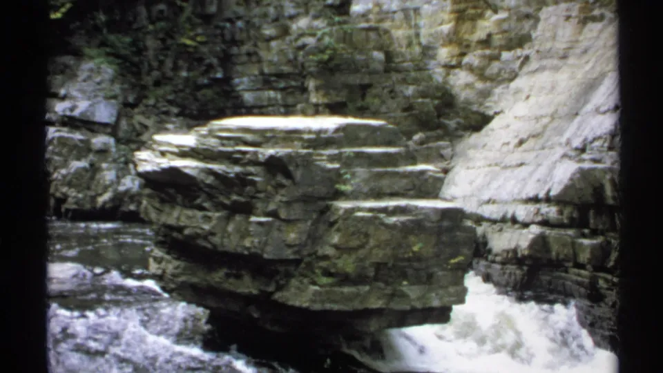 1971 New York 8mm frame showing white water cascading beside a broad layered boulder in a rocky gorge.