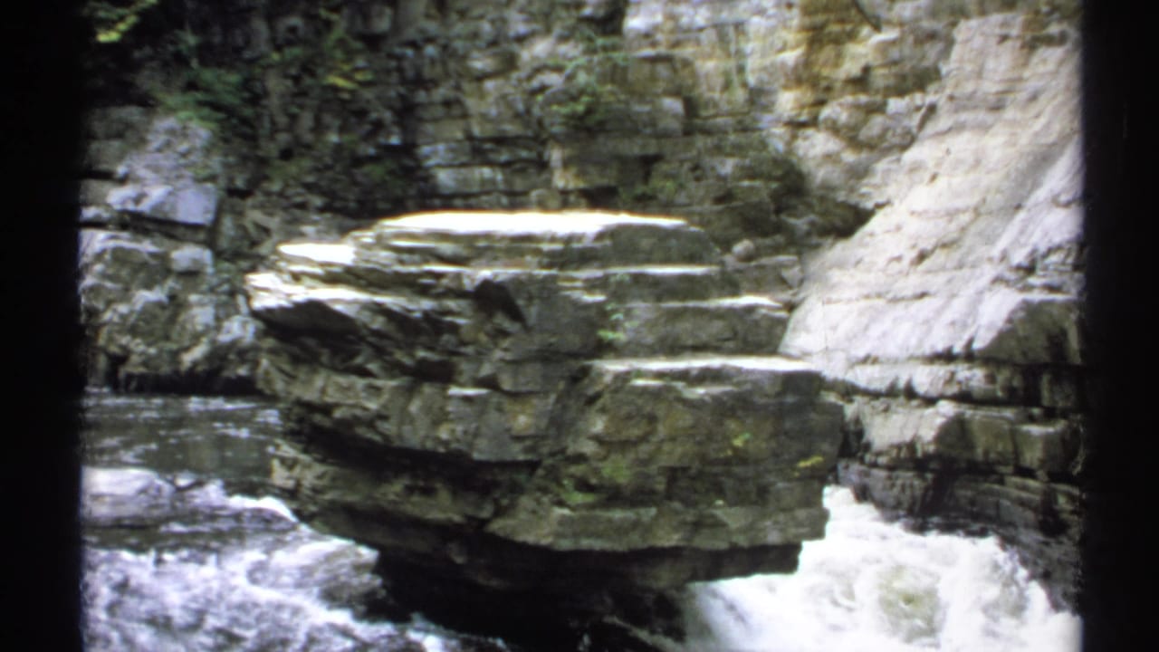 Large rock ledge above rushing water with steep canyon stone behind it.