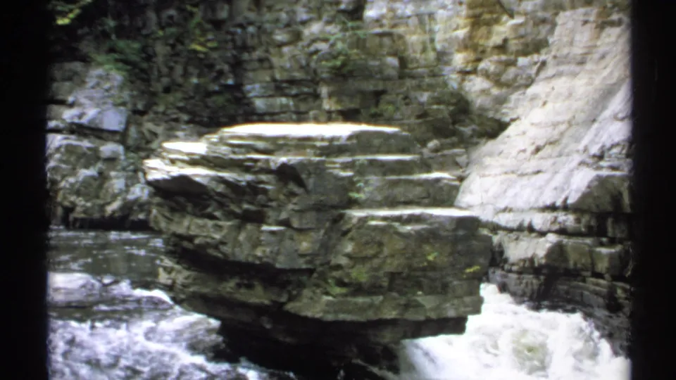 1971 New York 8mm frame of a broad boulder and fast water framed by rough gorge walls.