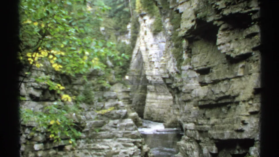 1971 New York 8mm frame looking down a leafy stone gorge with water running between rock walls.