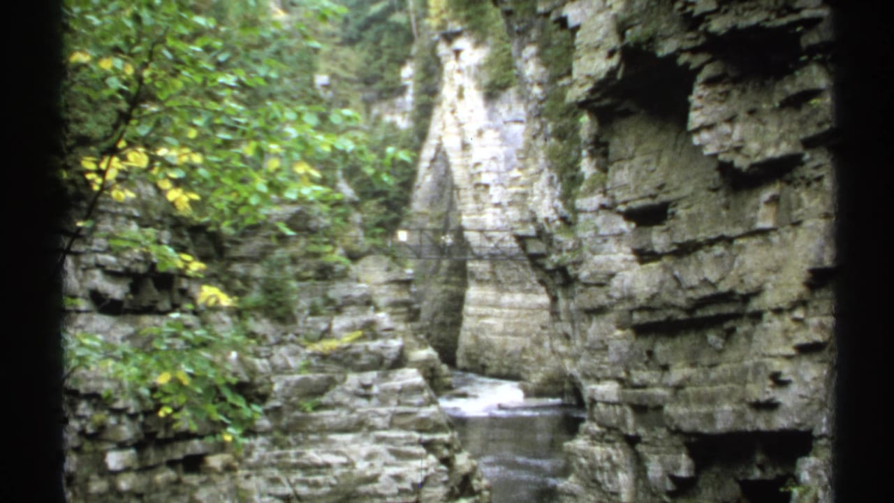 Similar gorge view with rock walls, trees, water, and bridge.