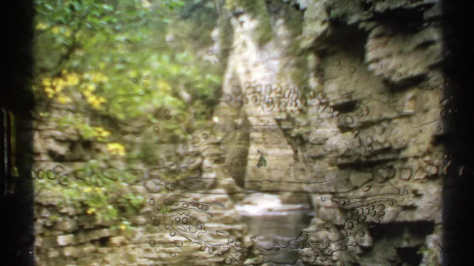 A softer 1971 8mm frame of the New York gorge shows foliage, rock walls, water below, and visible film artifacts across the image.