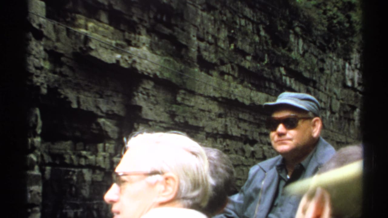 Tourists stand in a narrow rock gorge with a man in a blue cap and sunglasses near the center.