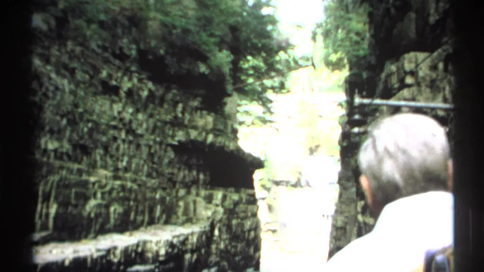 1971 New York 8mm frame with two visitors seen from behind while looking into a limestone gorge and bright stream channel.
