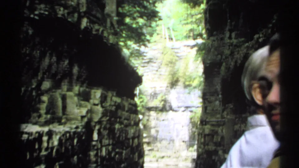 1971 New York 8mm frame with a partial visitor face at right, layered limestone cliffs, and a bright stream through the gorge.