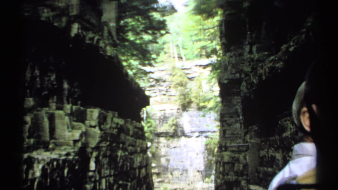 Shaded river canyon with layered rock walls and water beyond a dark foreground edge.