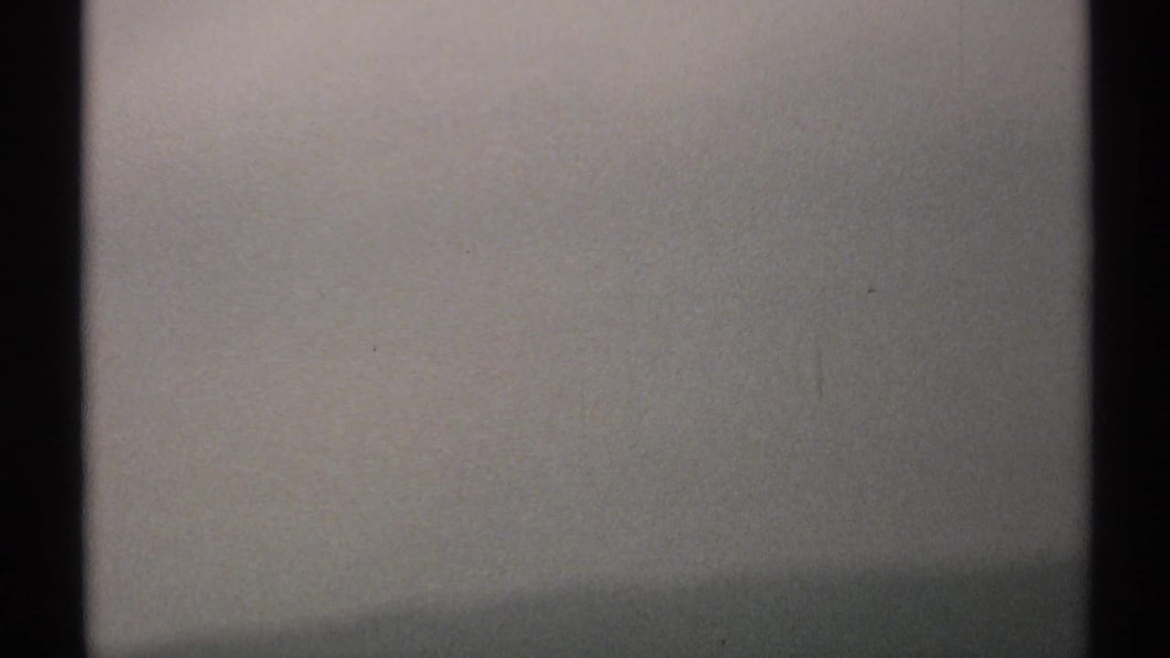 1971 New York 8mm frame showing a pale grey sky through dark window framing, with grain and soft exposure.