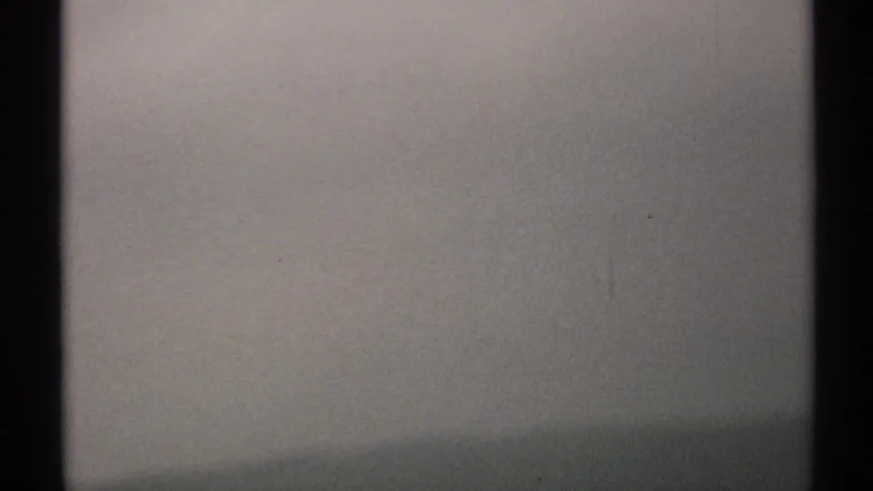 1971 New York 8mm frame showing a pale grey sky through dark window framing, with grain and soft exposure.