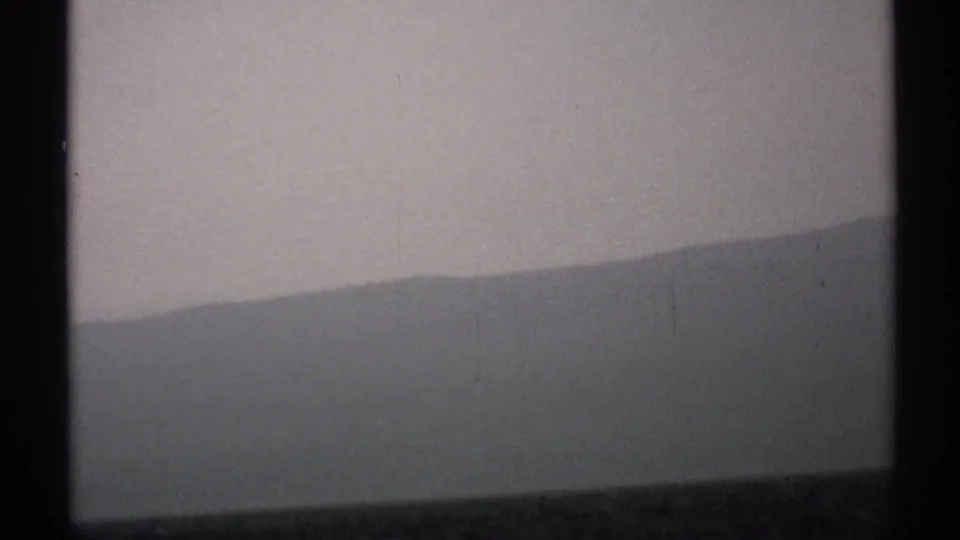 1971 New York 8mm view of a shadowed mountain ridge under a heavy grey sky, divided by dark window mullions.