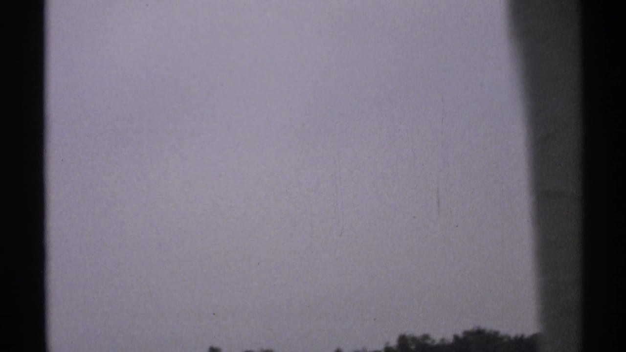 1971 8mm New York coastal footage begins with a muted sky and low distant treeline framed by dark window or structural edges.