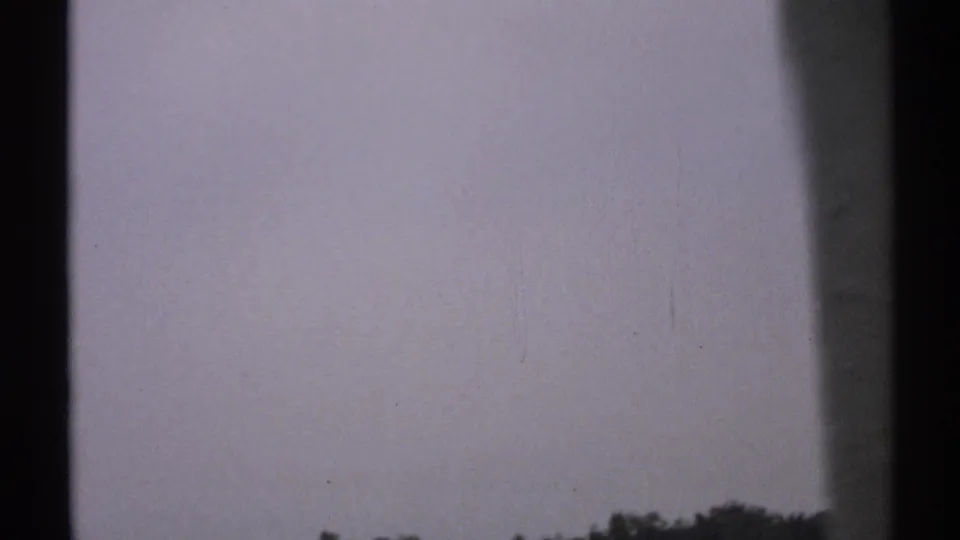 1971 8mm New York coastal footage begins with a muted sky and low distant treeline framed by dark window or structural edges.