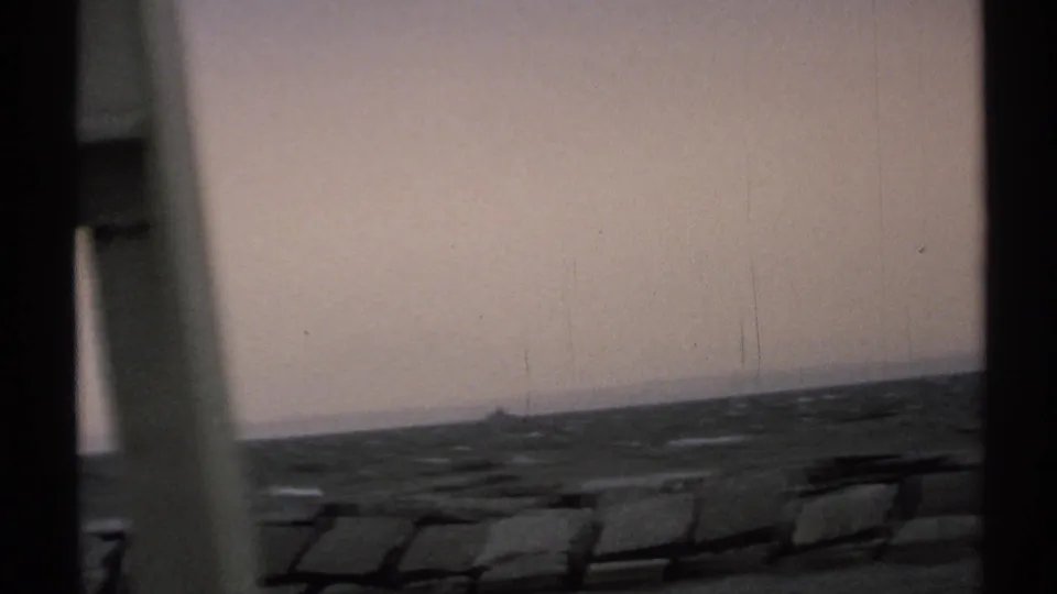 A New York shoreline view shows rough water, a small boat on the horizon, and dark window framing at the side of the 8mm frame.