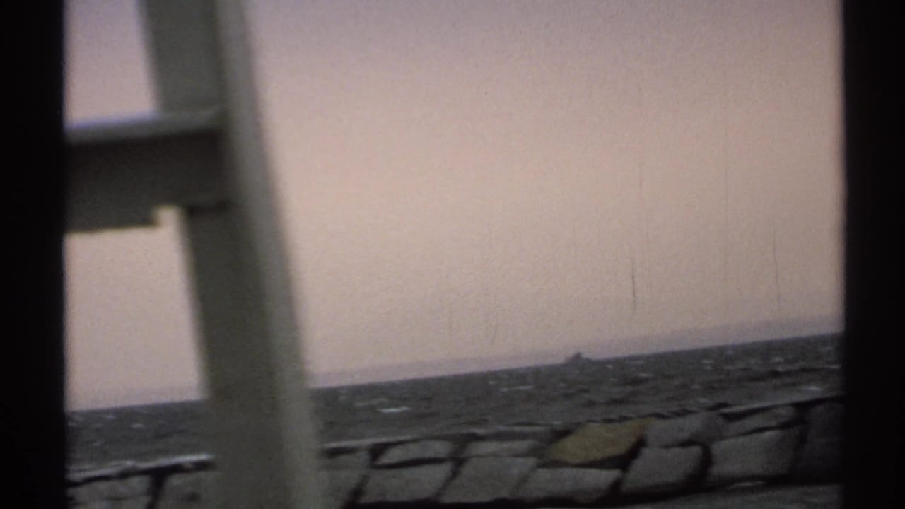 Boat-framed view of open water, low shoreline, and a distant dark marker under a muted sky.