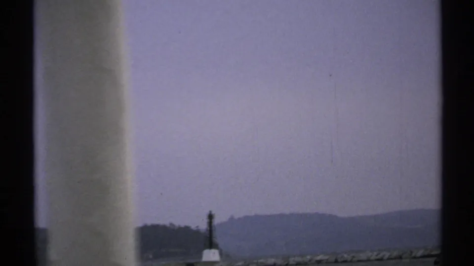 1971 8mm boat footage with pale foreground structure, distant shoreline, and a small dark marker near the waterline.