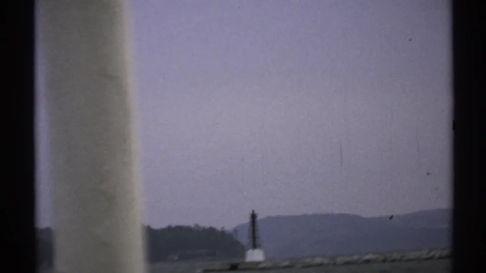 1971 New York 8mm frame of a coastal horizon, dark marker, low land, and distant hills seen from a boat.