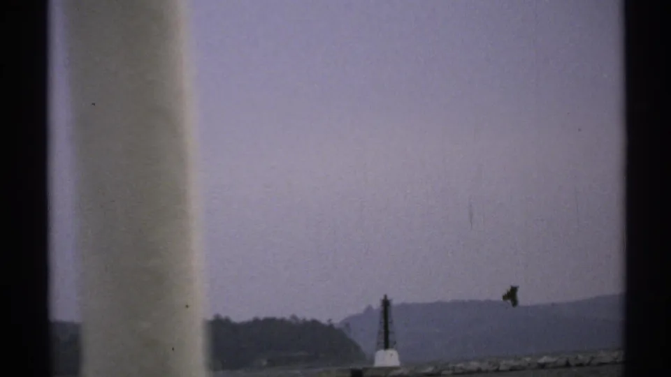 1971 New York home-movie frame showing water, distant shoreline, and a small boat, partly obscured by dark film-frame borders.