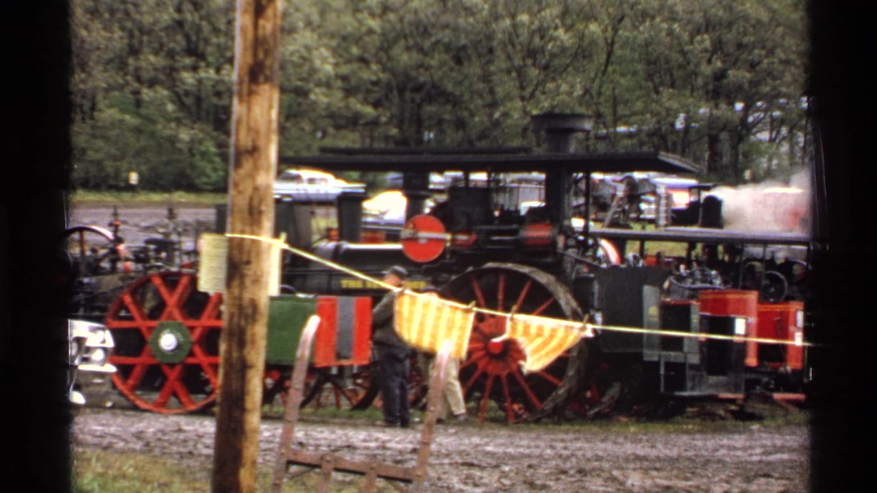 1971 Rollag, Minnesota 8mm frame showing a black steam engine with red wheels, spectators, and yellow checkered cloth in front.
