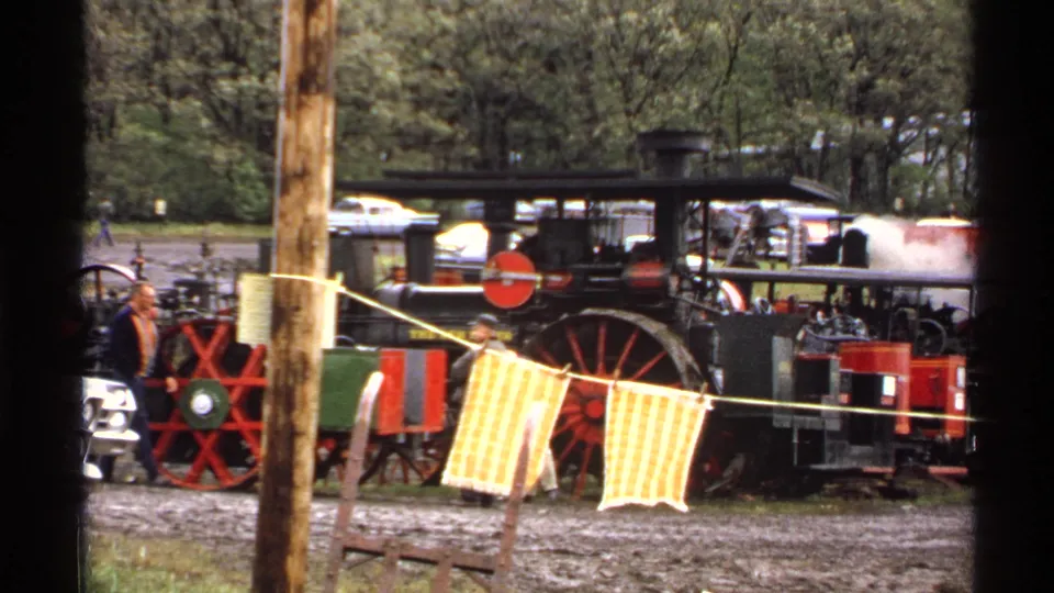 Rollag, Minnesota 1971 frame with visitors near a black steam engine, red wheels, and yellow cloth across the view.