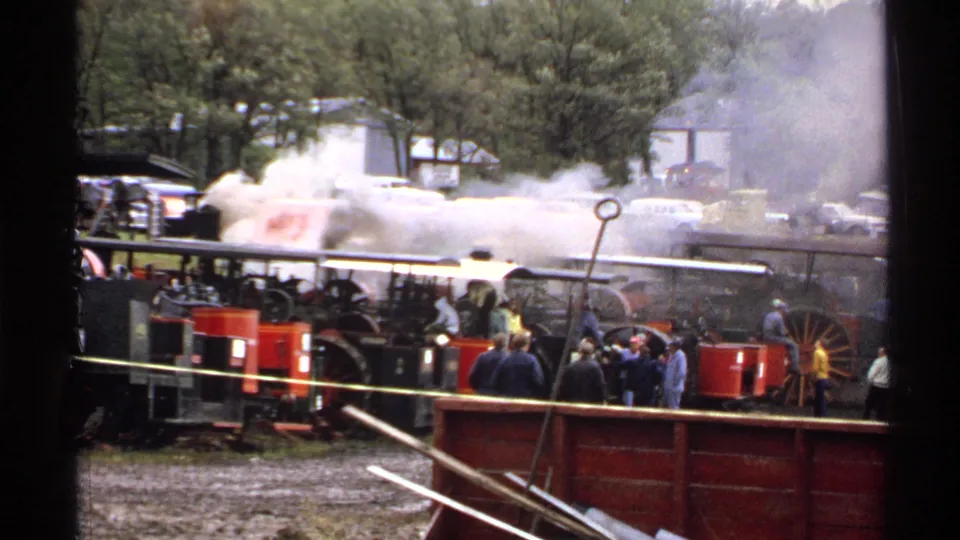 1971 Rollag 8mm frame showing steam spreading over a crowded railway demonstration area with red machinery below.