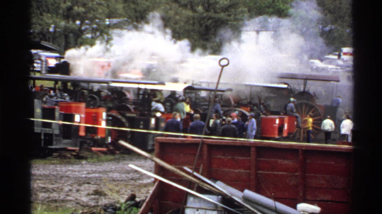 Crowd watches steam-powered machines releasing smoke outdoors.