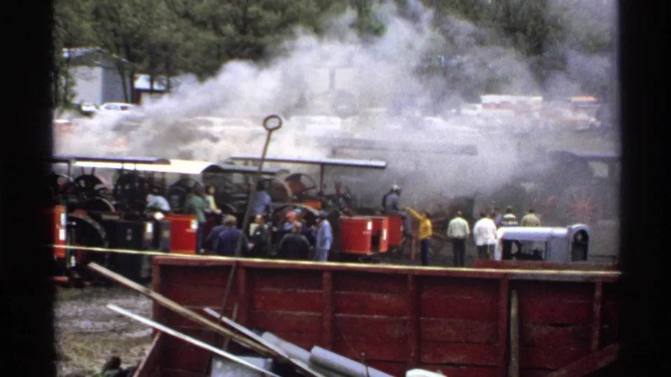 1971 8mm frame from Rollag showing thick smoke over a steam engine display with spectators and parked cars behind it.