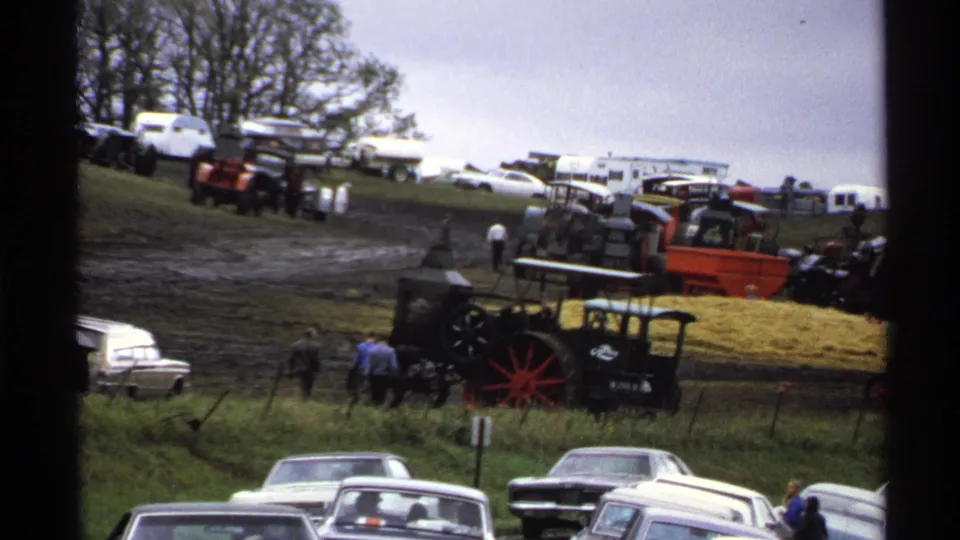Wide 1971 Rollag, Minnesota 8mm view of antique tractor show grounds with steam equipment, spectators, muddy tracks, and parked cars.