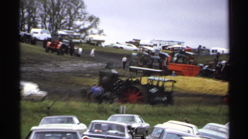 1971 Rollag, Minnesota frame with foreground cars, antique tractors, hay bales, trailers, and people moving through a rural exhibit area.