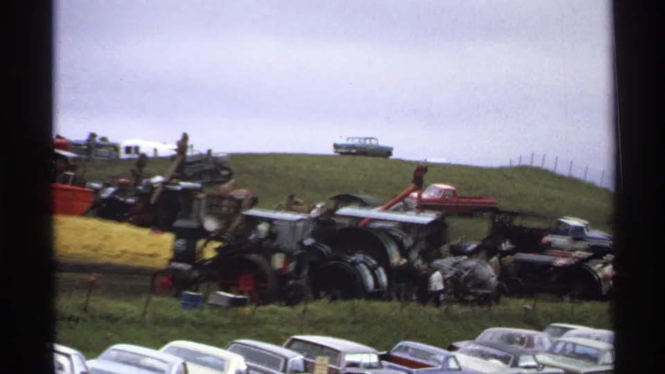 1971 Rollag, Minnesota home-movie still showing steam tractors, parked classic cars, a hay bale area, and visitors at an agricultural show.