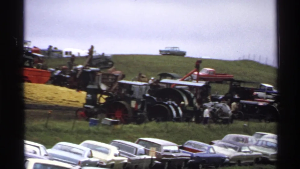 1971 Rollag, Minnesota frame showing steam tractors, farm machinery, visitors, and classic cars at a rural agricultural display.