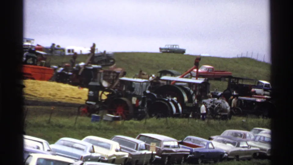 Rollag, Minnesota 1971 home-movie frame showing classic cars in front of antique tractors and farm machinery on a grassy hillside.