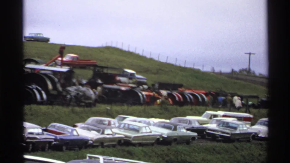 Home-movie frame from Rollag, Minnesota in 1971 with antique farm machinery and classic cars at a rural fairground.