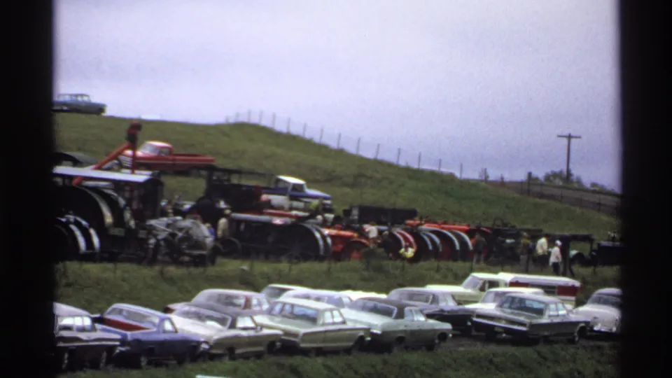 Rollag, Minnesota 1971 8mm frame showing visitors near antique tractors, farm machinery, and classic cars under an overcast sky.