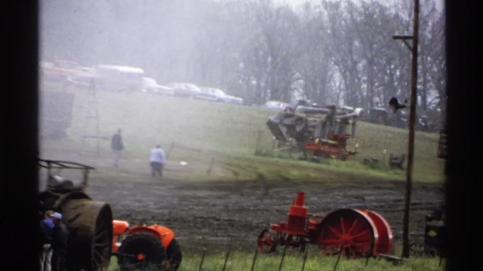 Soft 8mm footage shows a misty Rollag fair field with vintage tractors, red equipment, walking visitors, and cars above the slope.